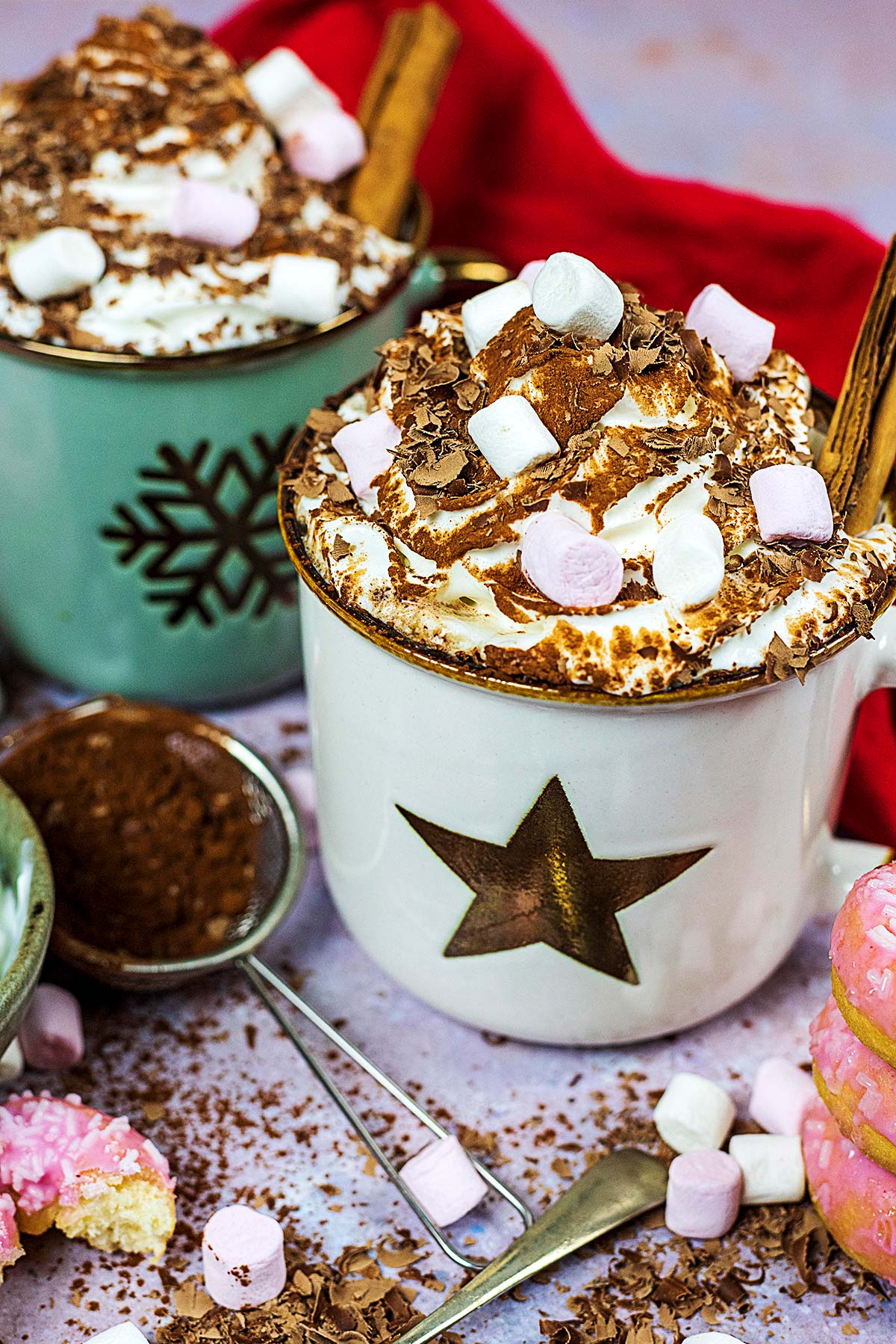 Two festive mugs topped with whipped cream, marshmallows and cocoa powder.