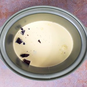 A slow cooker bowl containing milk, cream and chunks of chocolate.