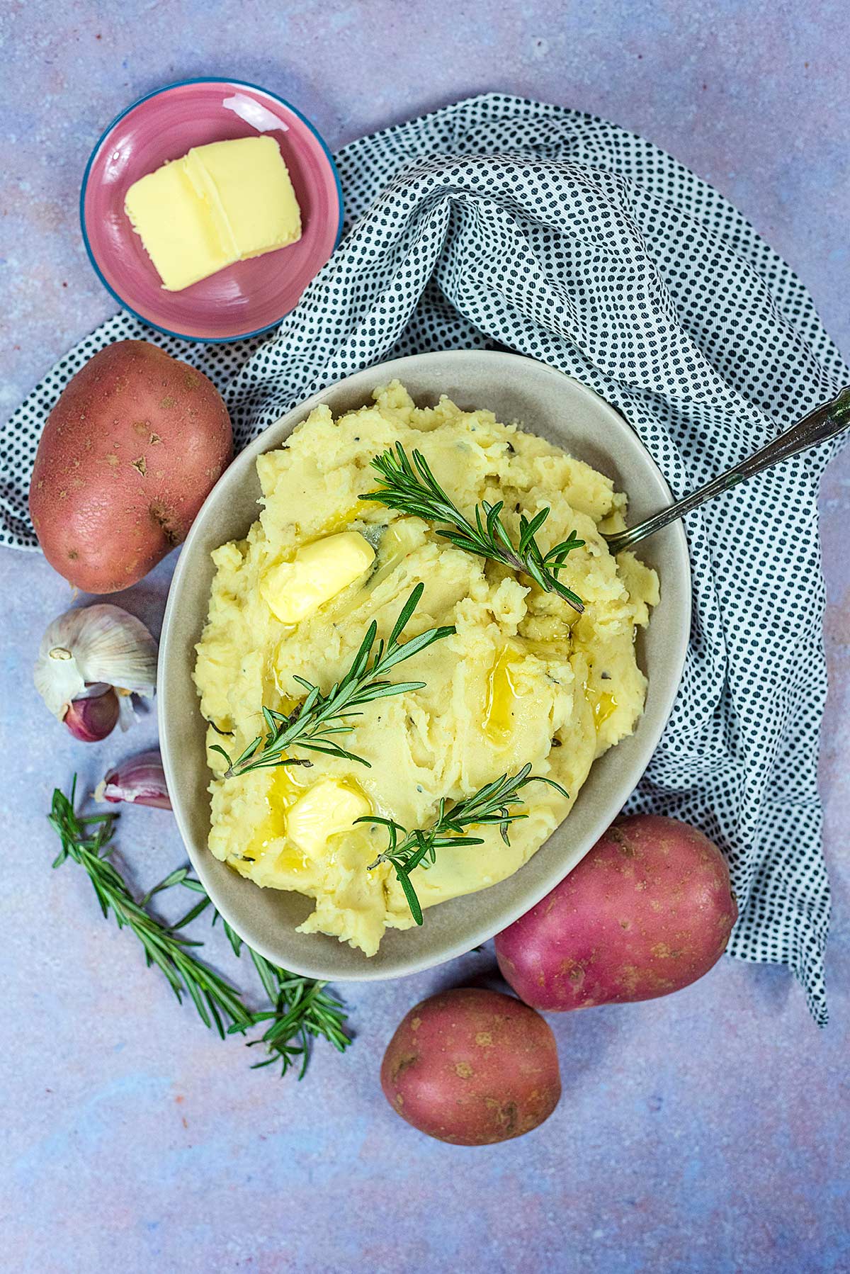 A bowl of slow cooker mashed potato next to some whole potatoes.