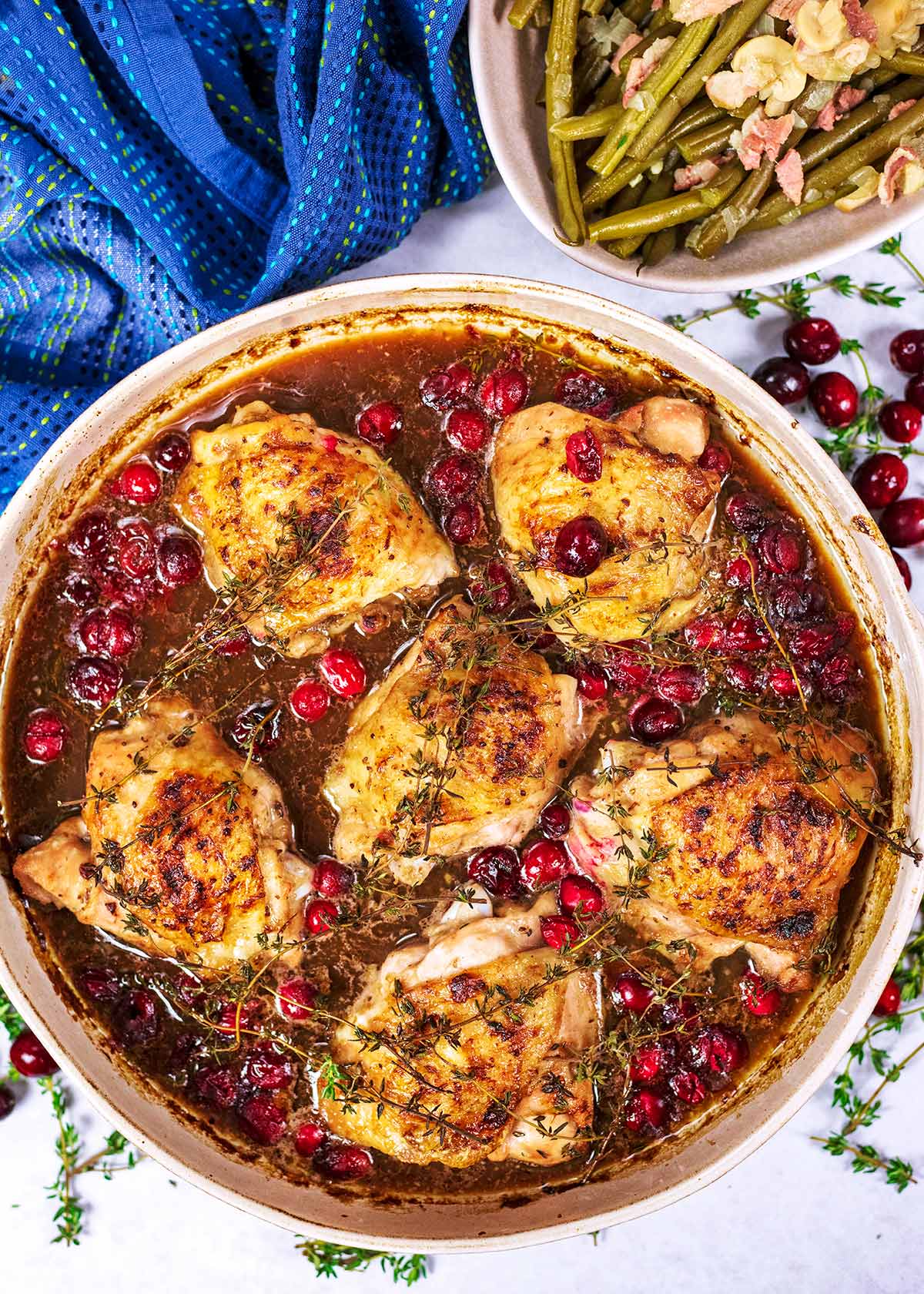 A large round dish containing cooked chicken thighs in a cranberry gravy.