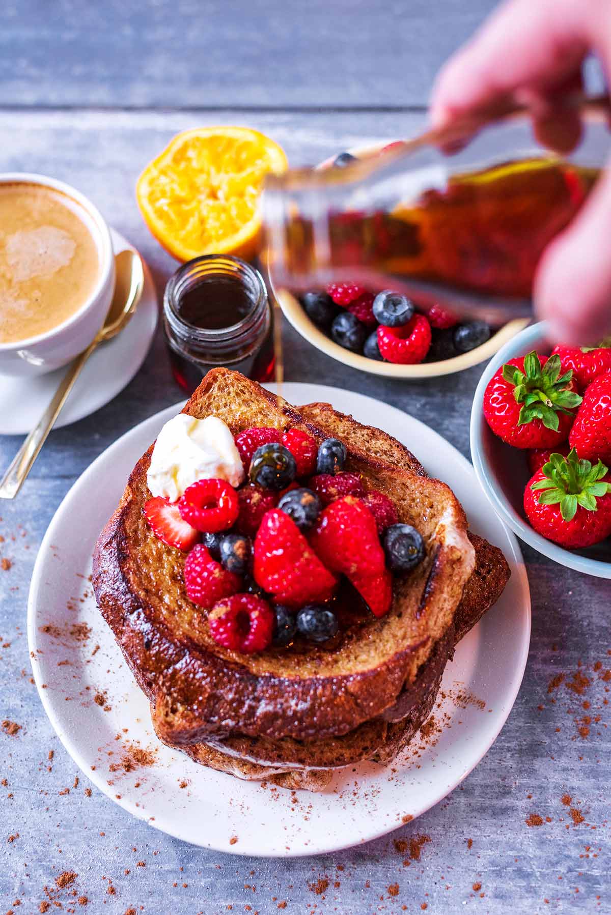 Maple syrup being poured from a bottle onto some French toast.