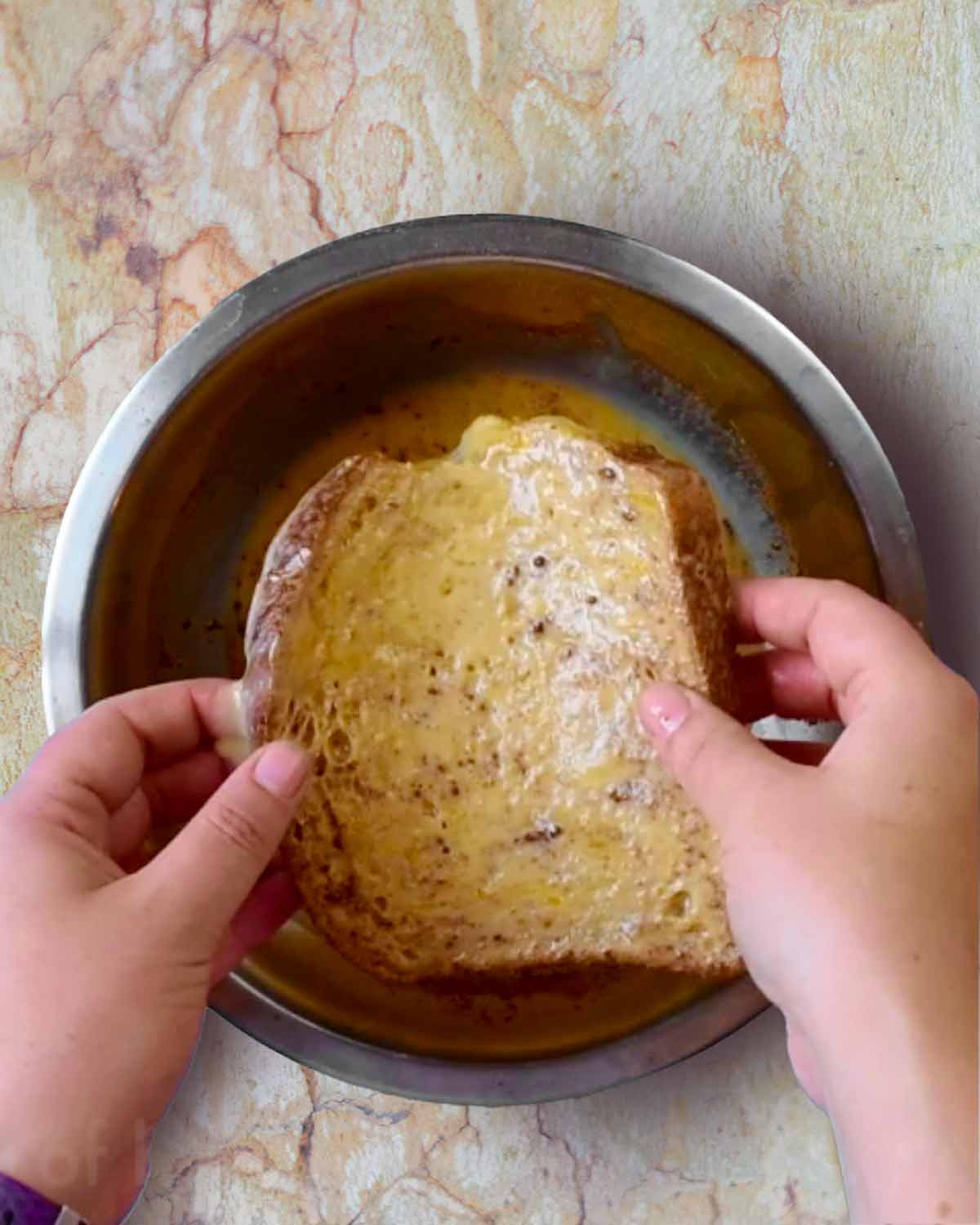 A slice of bread being dipped into a bowl of egg mixture