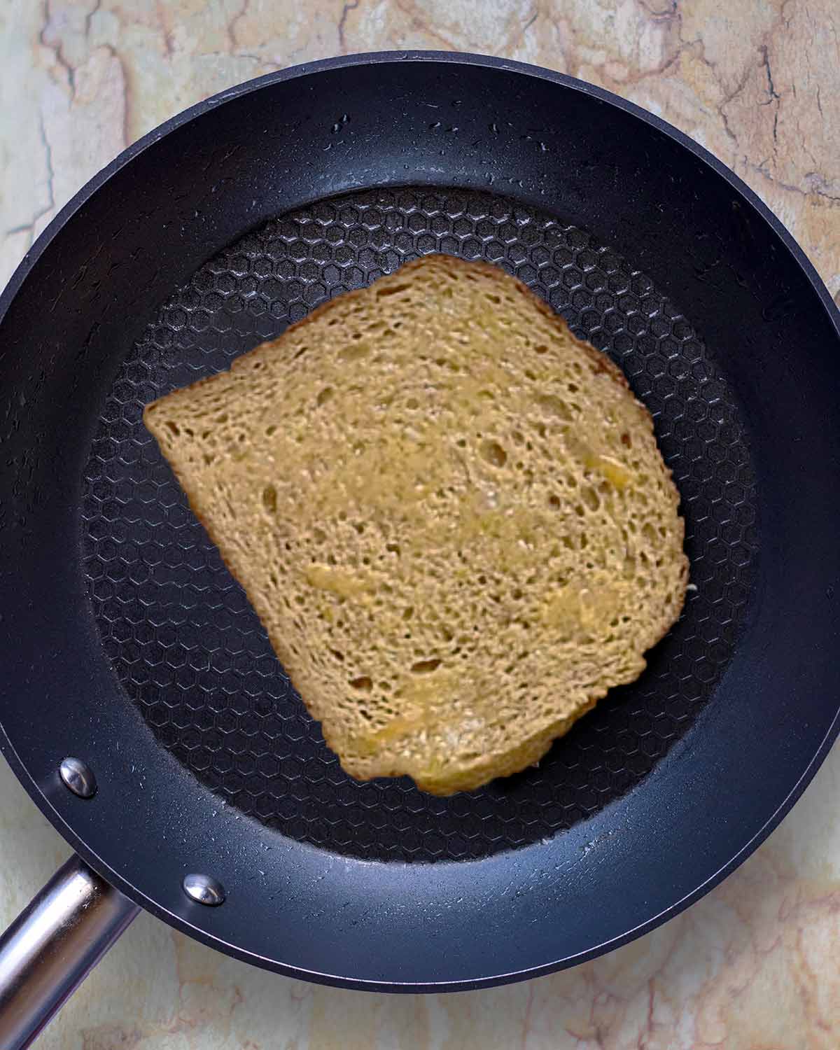 A slice of French toast cooking in a frying pan.