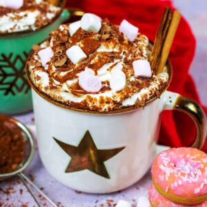 Slow cooker hot chocolate next to a red towel and a stack of pink doughnuts.