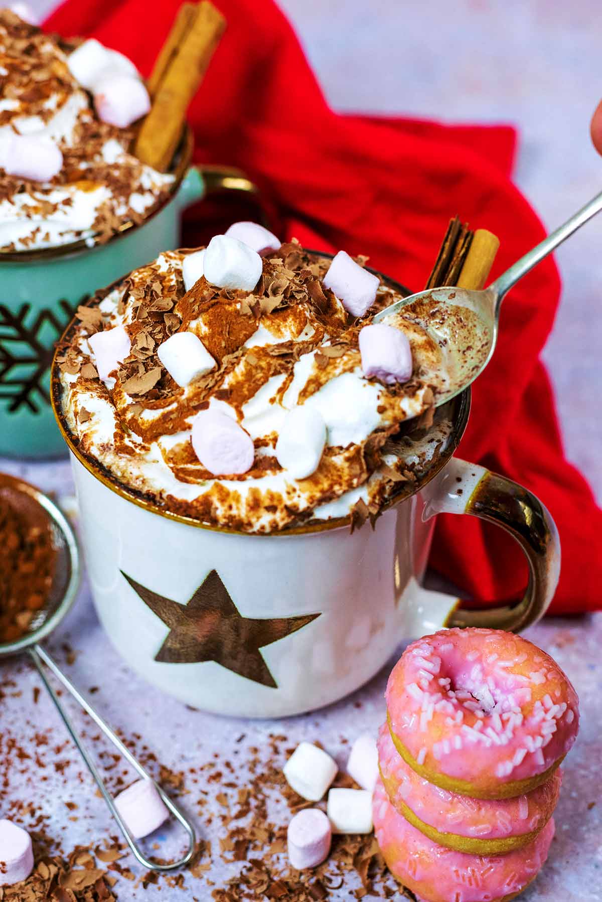 A spoon lifting out some cream from a mug of hot chocolate.