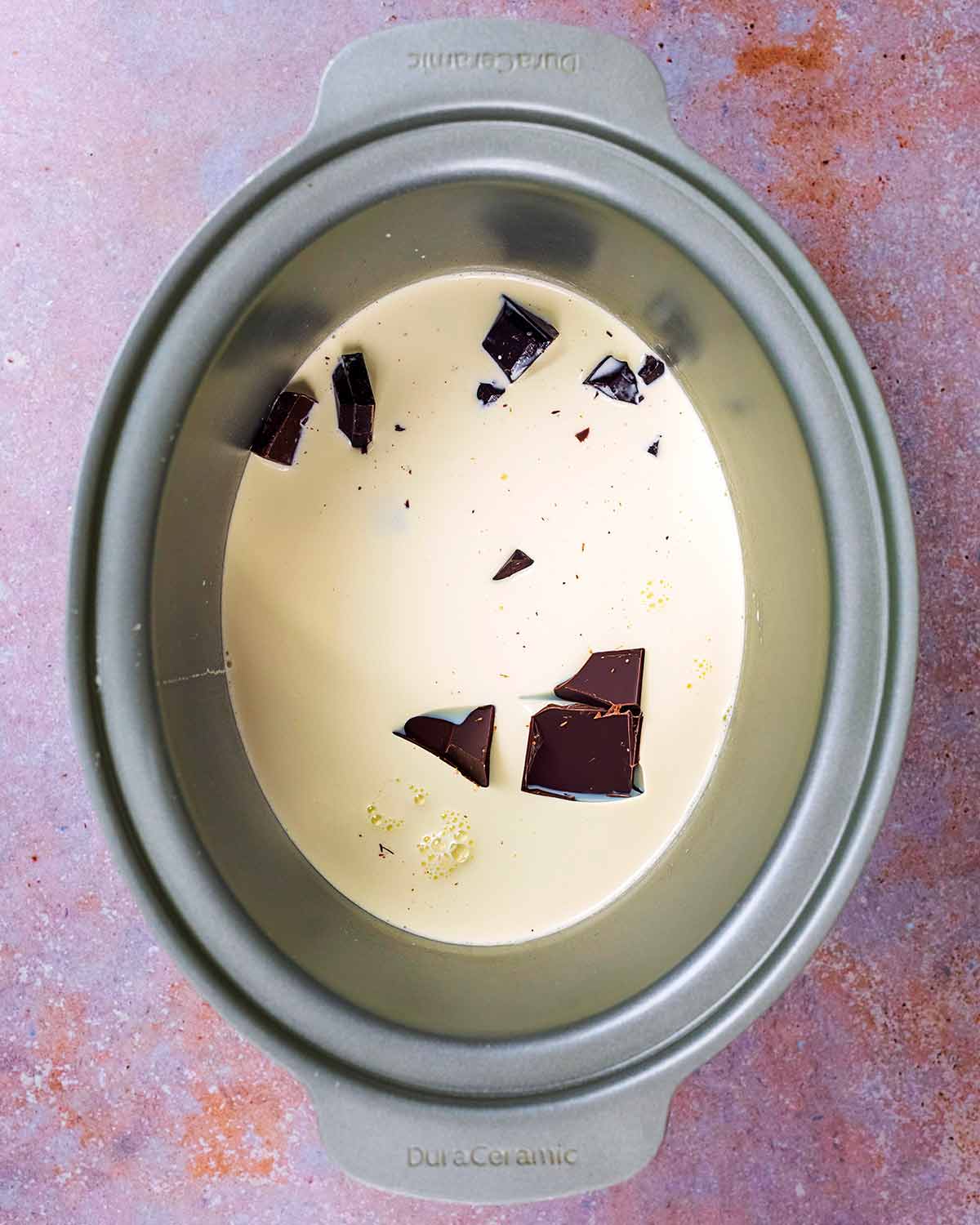 A slow cooker bowl containing milk, cream and chunks of chocolate.