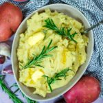 A bowl of Slow Cooker Mashed Potatoes with sprigs of rosemary on top.