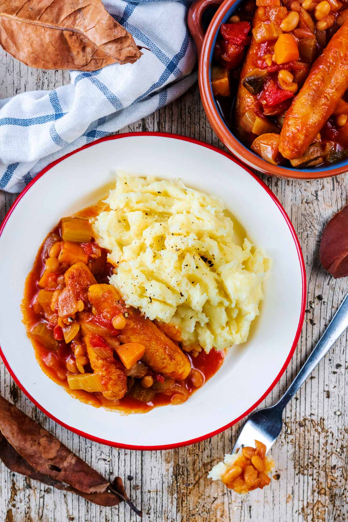Sausage casserole and mashed potato on a plate next to a large bowl of extra casserole.