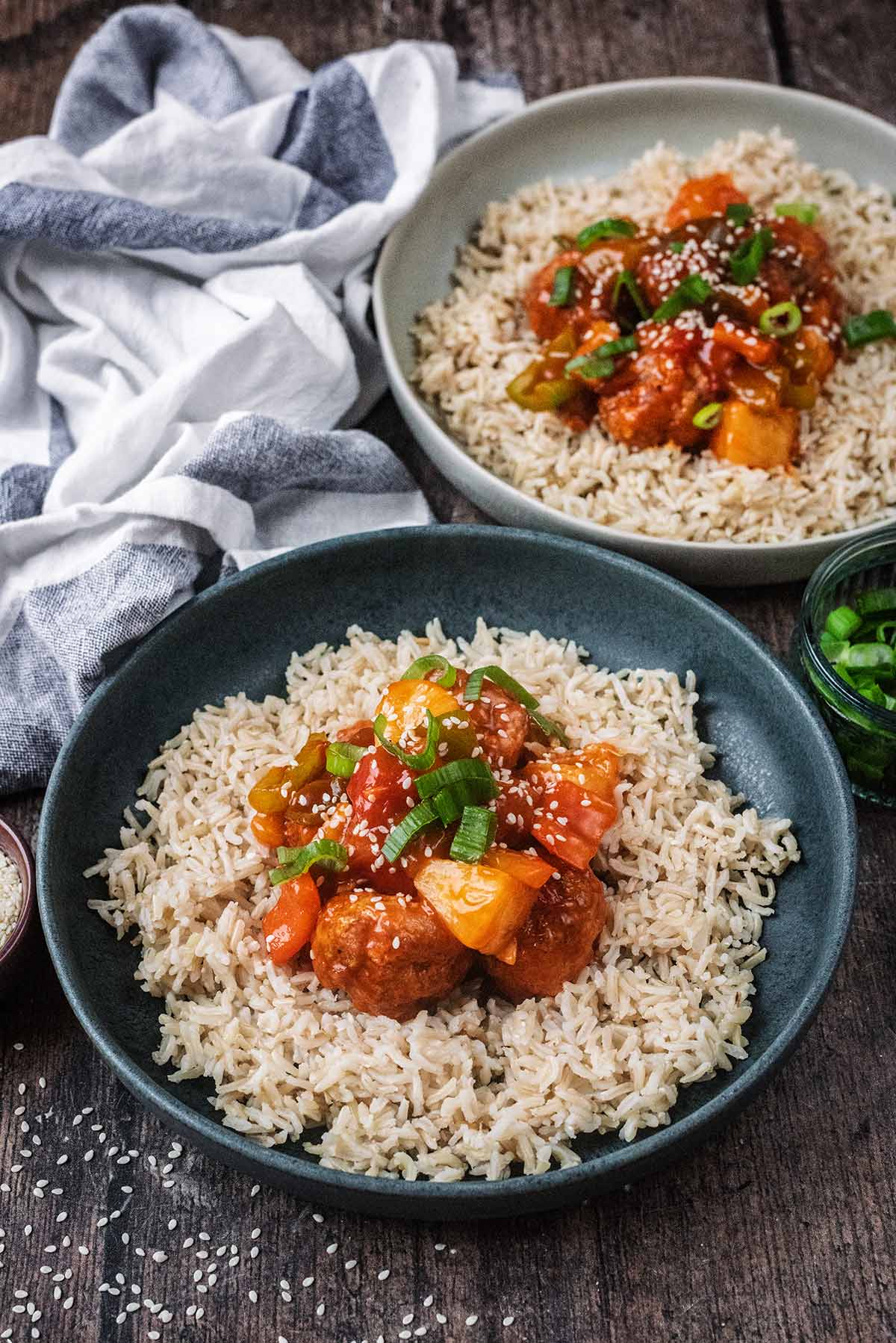 A bowl of sweet and sour meatballs and rice in front of another bowl of the same.