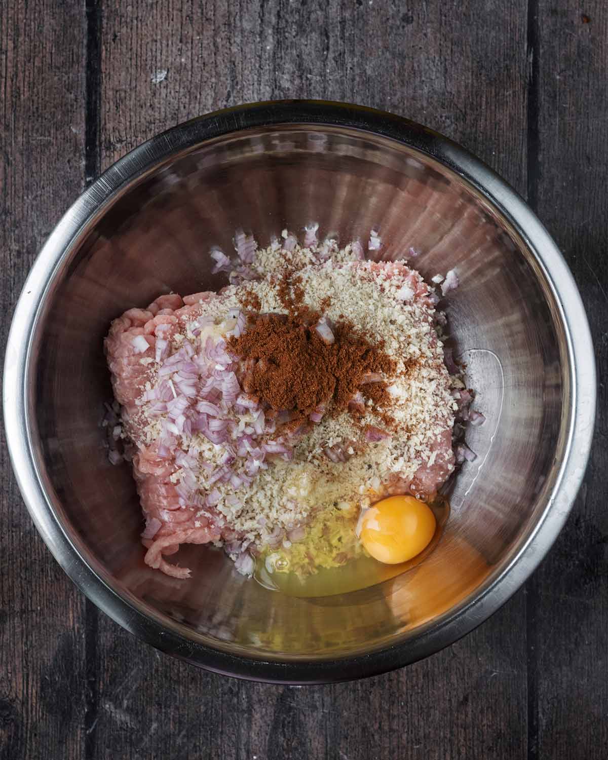 A mixing bowl containing chicken mince, chopped shallots, breadcrumbs, egg and Chinese 5 spice.