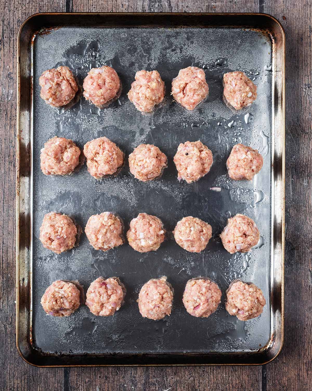 Twenty chicken meatballs on a baking tray, lightly coated with oil.