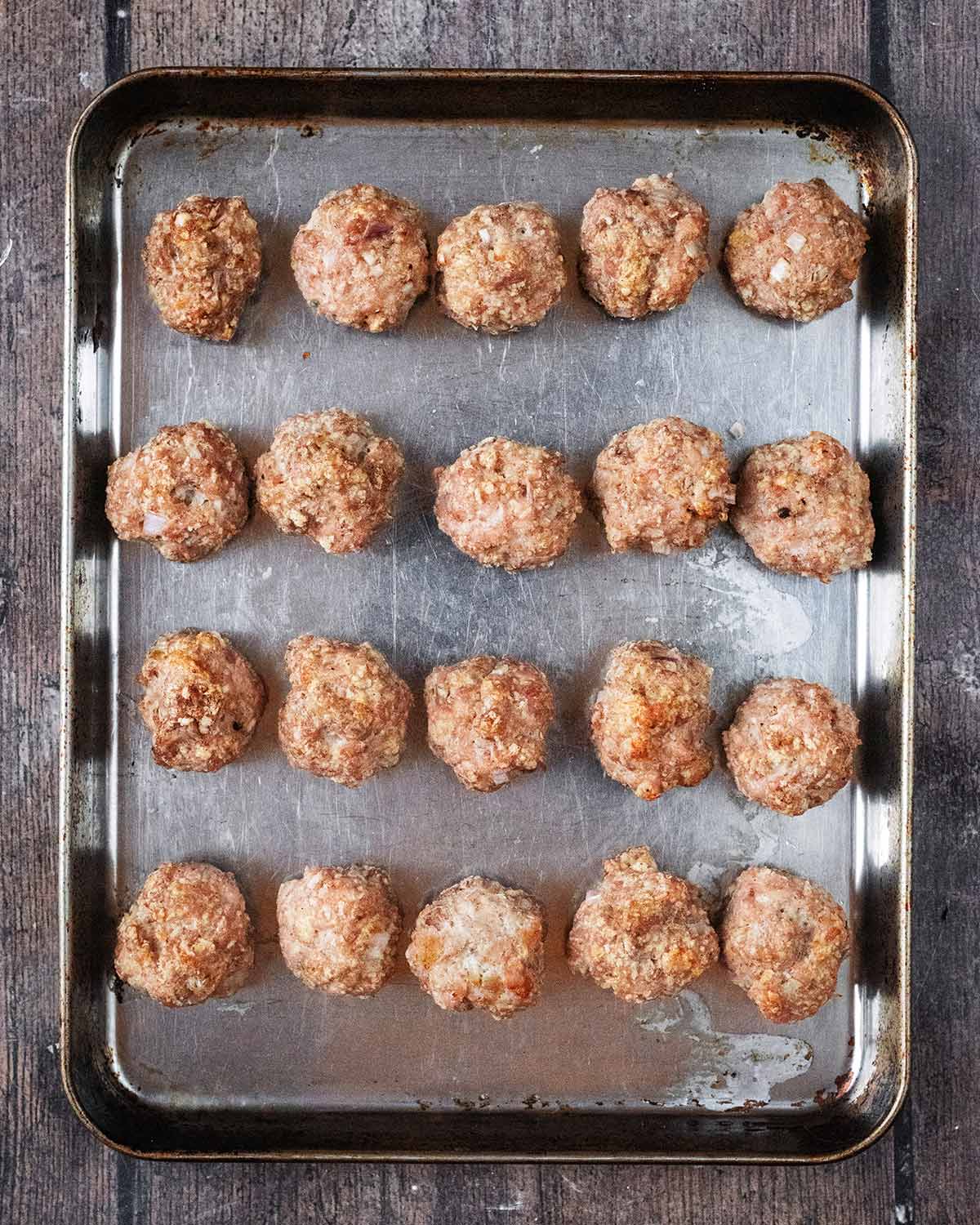 Twenty cooked chicken meatballs on a baking tray.