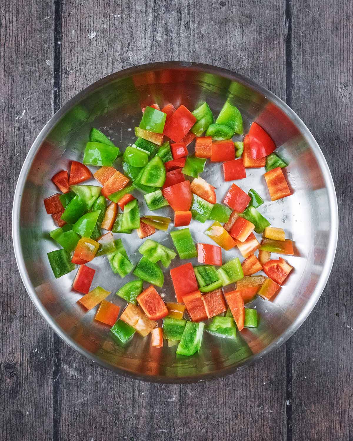 A frying pan with chunks of red and green bell pepper in it.