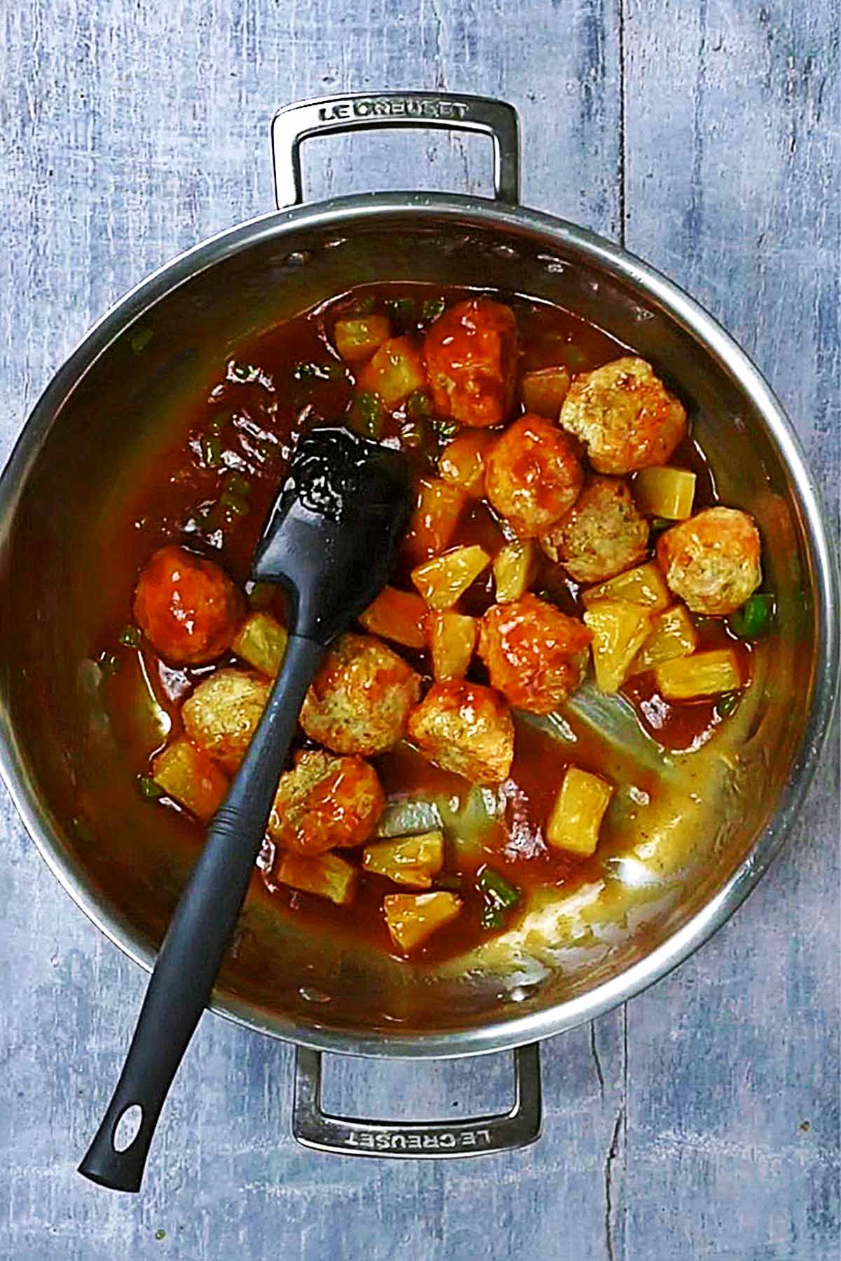 Meatballs, chopped peppers and pineapple chunks cooking in a sweet and sour sauce.