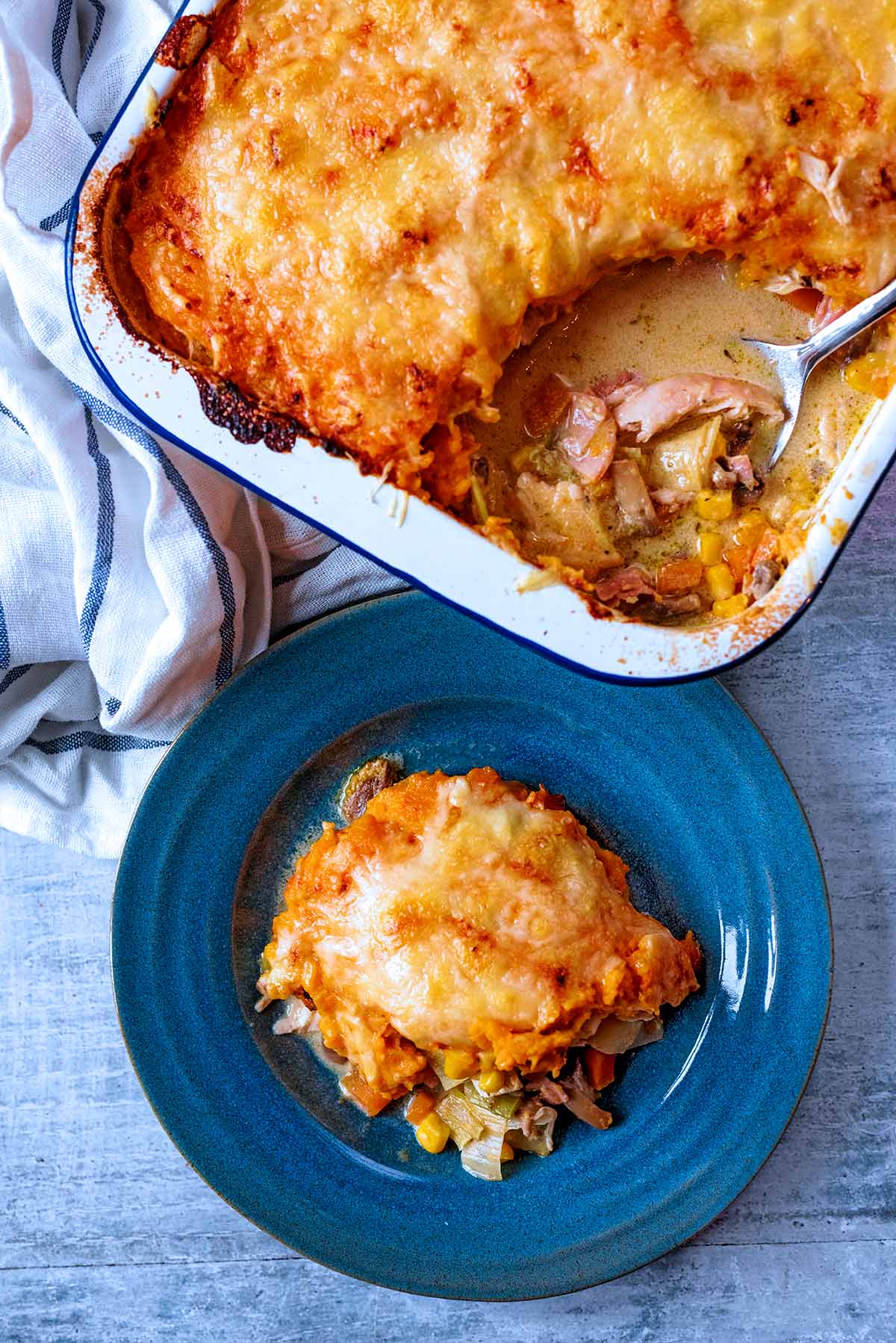 A baking dish containing turkey pie with a corner scooped out onto a plate.