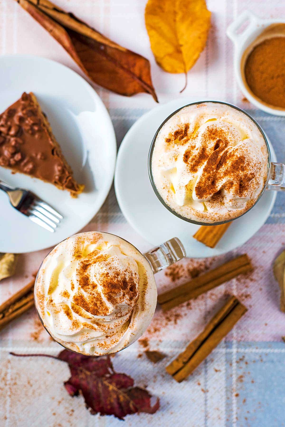 Two glasses of coffee, topped with cream and dusted with cinnamon. A slice of cake is next to them.