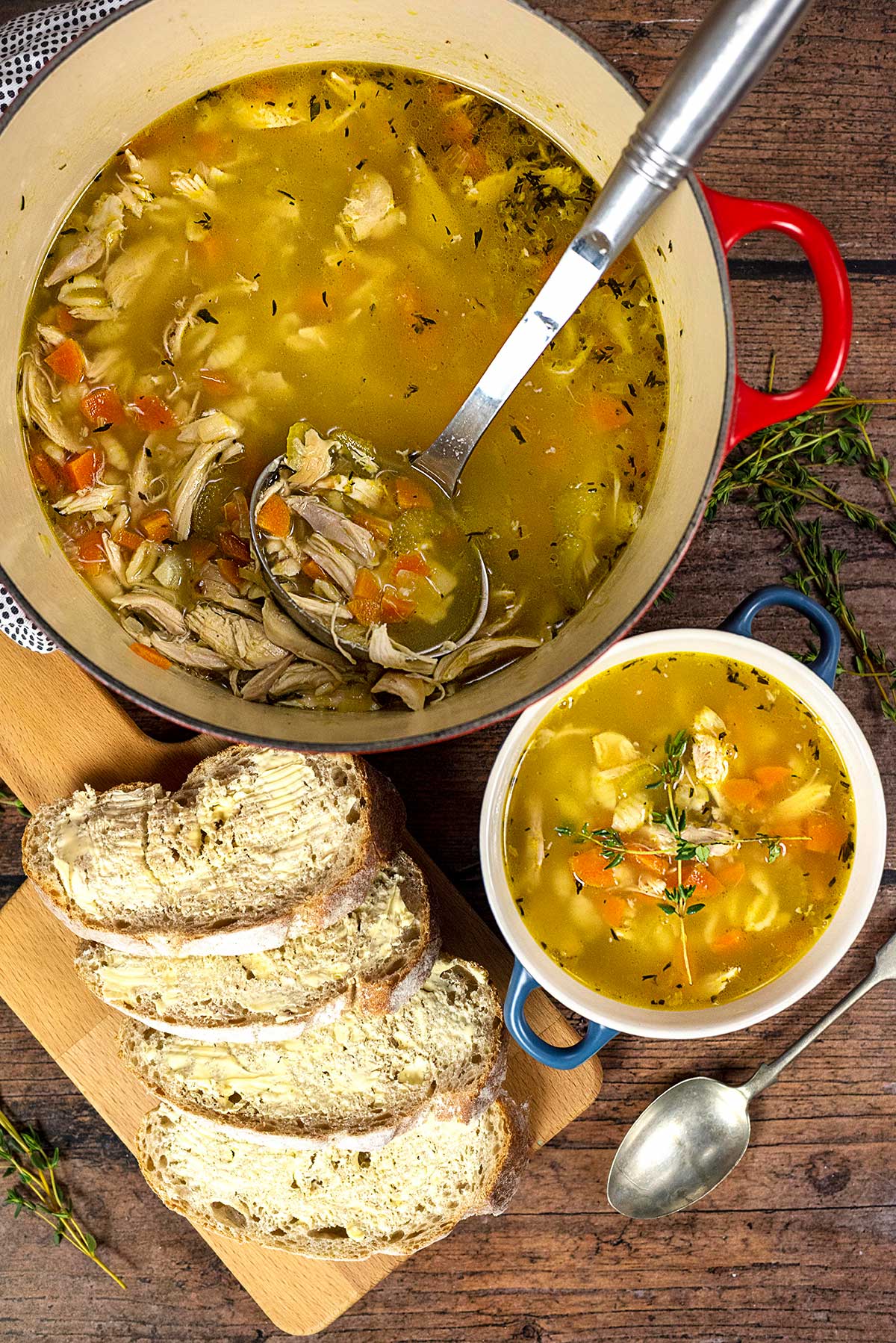 A large pan of turkey soup next to a bowl of soup and some slices of buttered bread.