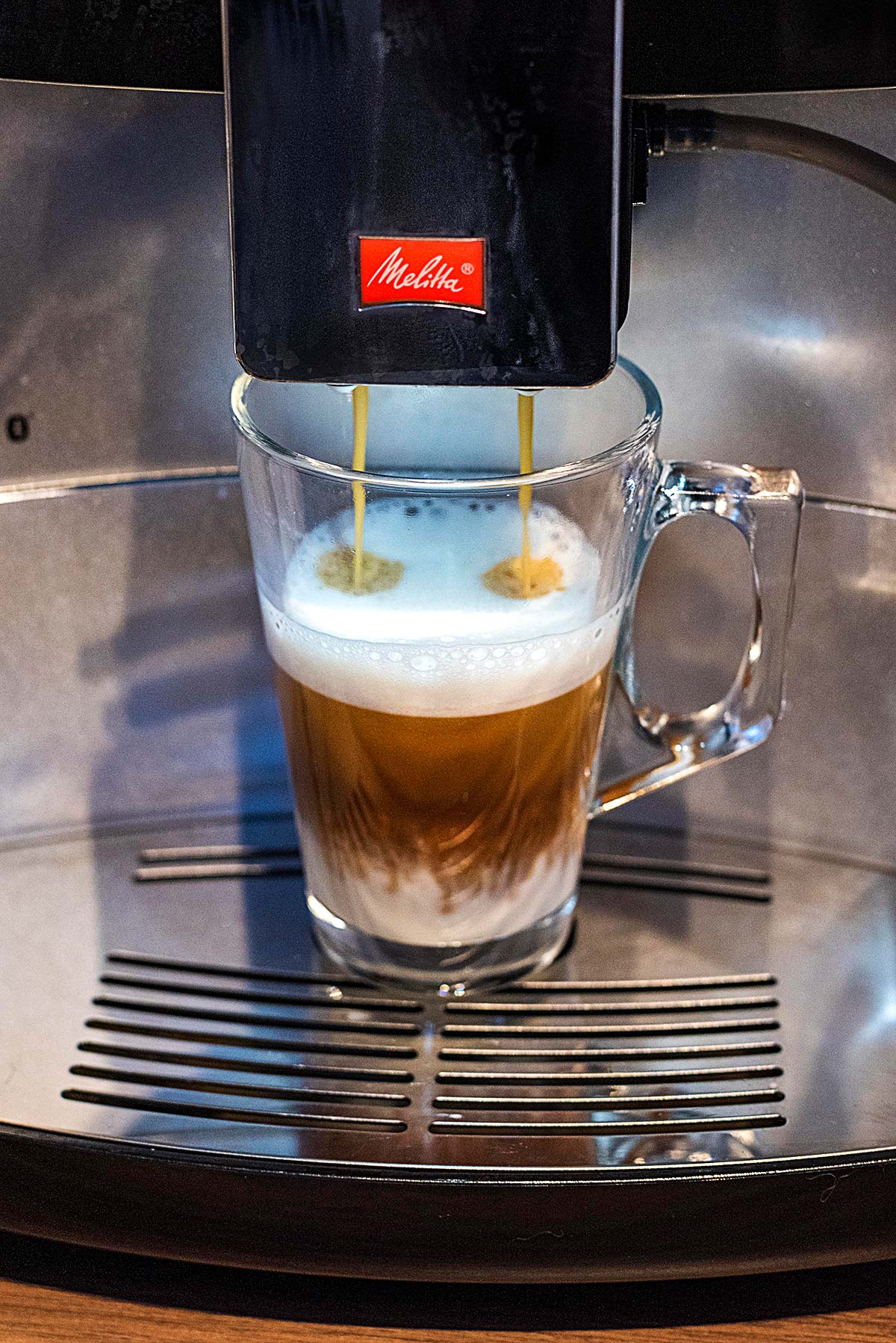 A latte glass being filled with coffee from a barista machine.