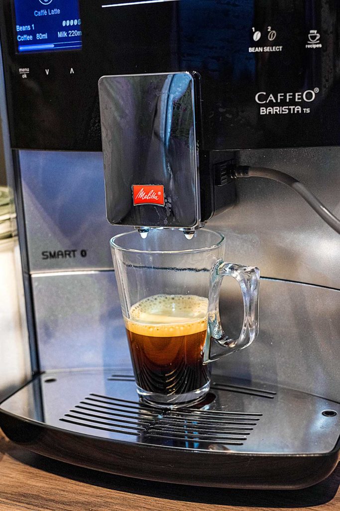 Coffee coming out of a barista machine into a latte glass.