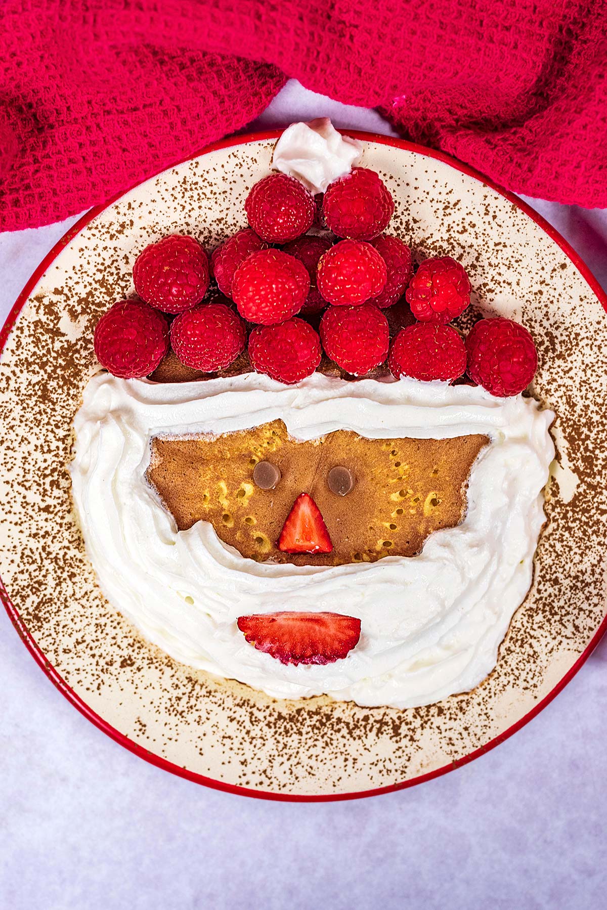 A Santa Claus pancake with raspberries for a hat and strawberry mouth and nose.