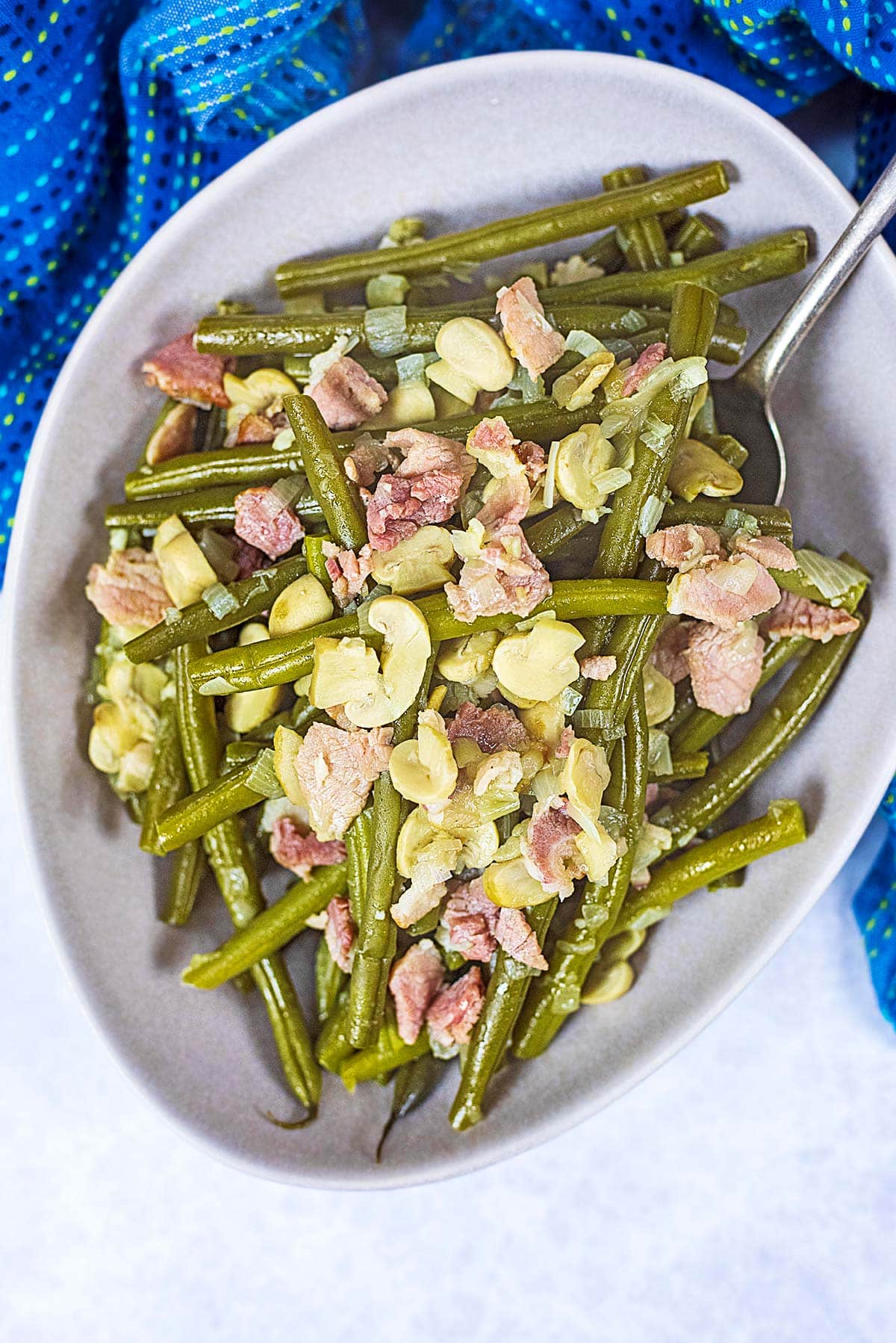 A bowl of green beans mixed with chopped bacon and sliced mushrooms.