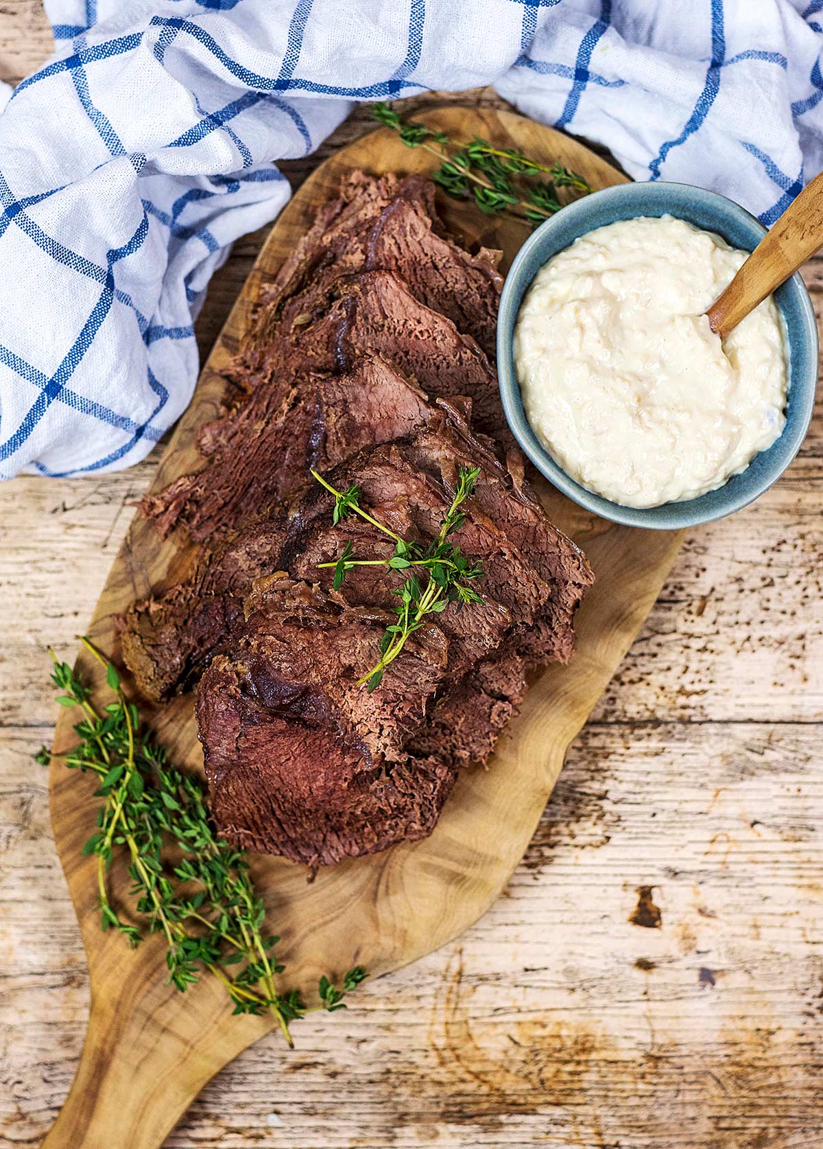 Slices of roast beef on a wooden serving board with a bowl of horseradish sauce.