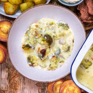 A plate of broccoli cheese next to roast potatoes and Yorkshire puddings.