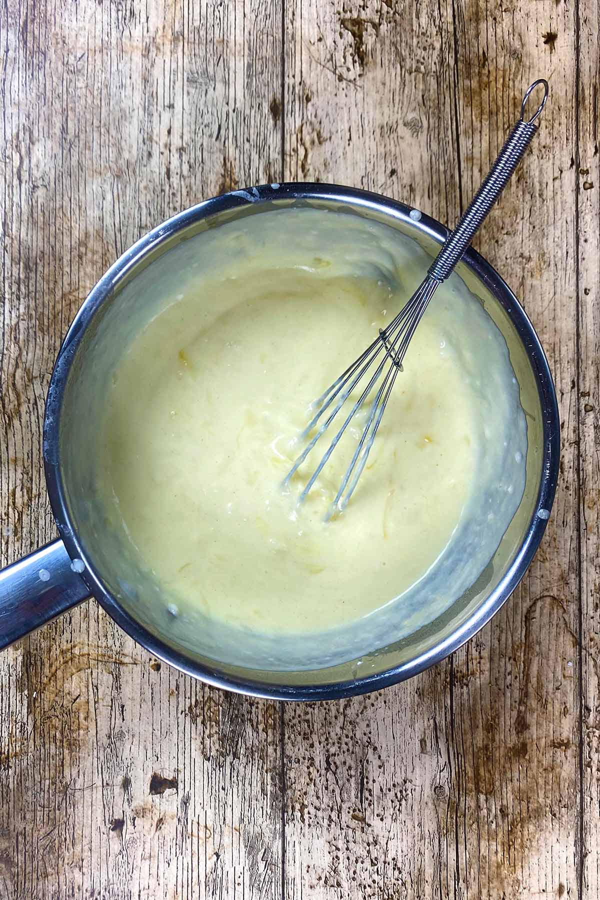 A pan of cheese sauce with a whisk in it.