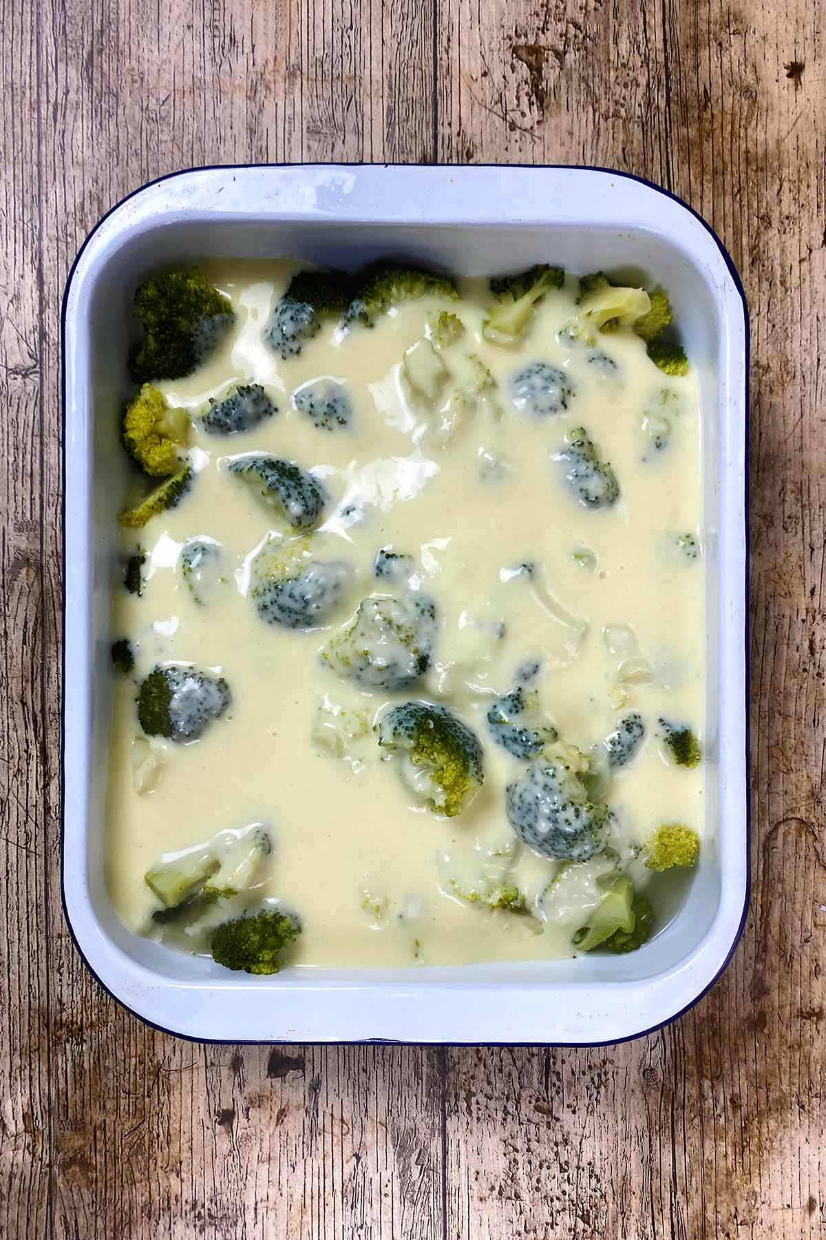 A rectangular baking dish full of broccoli florets covered in cheese sauce.