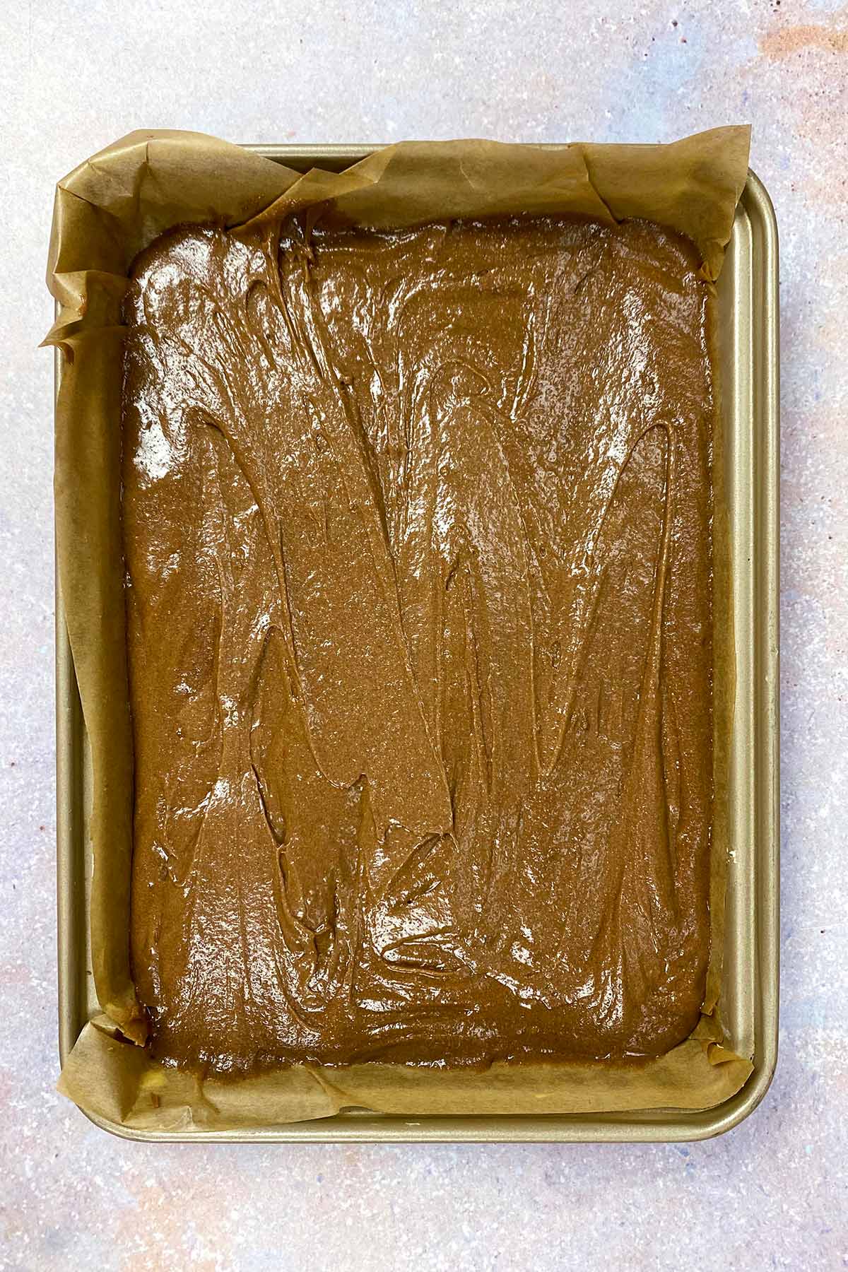 Brownie batter poured into a lined baking tray.