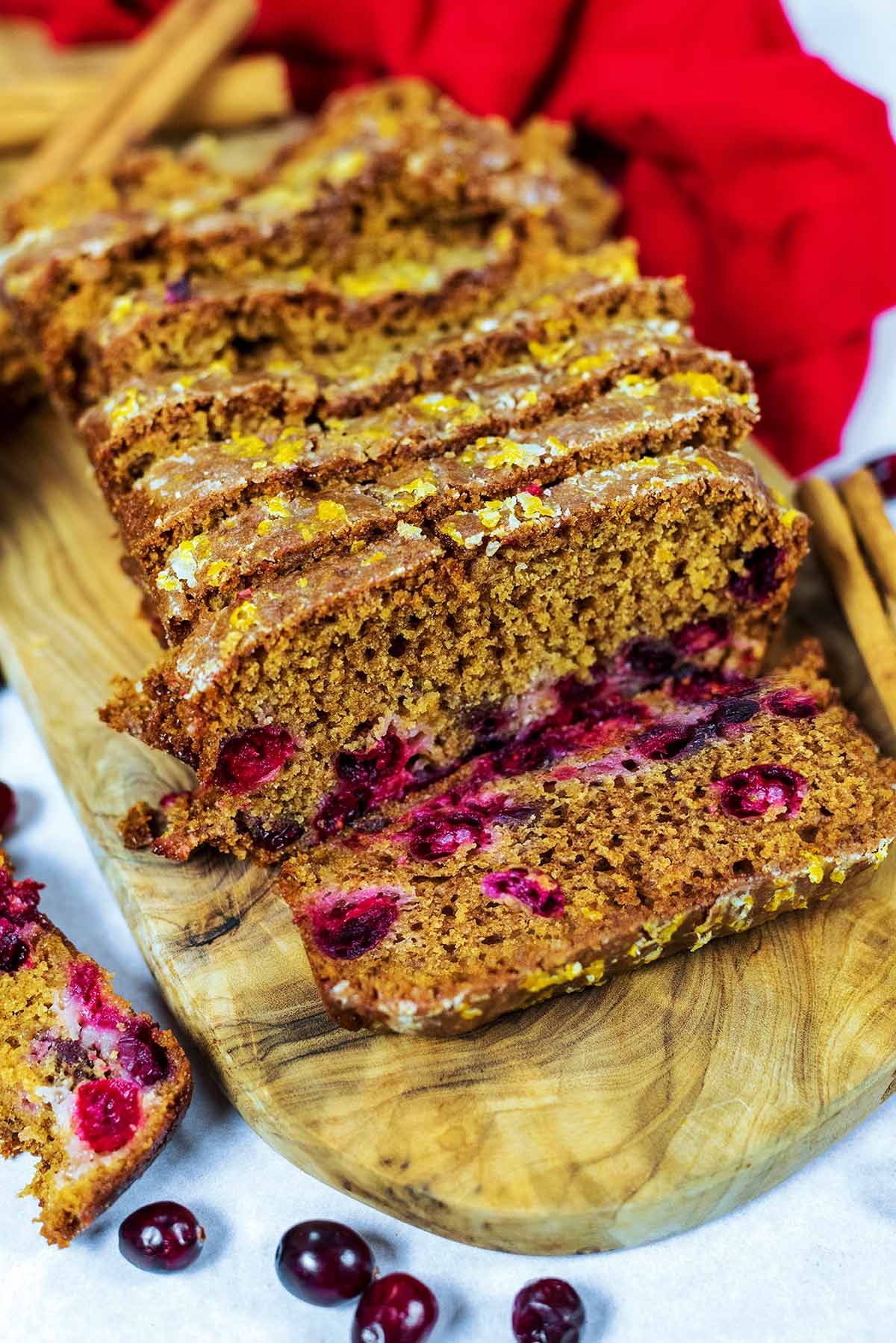 Slices of cranberry loaf on a board next to a red towel.
