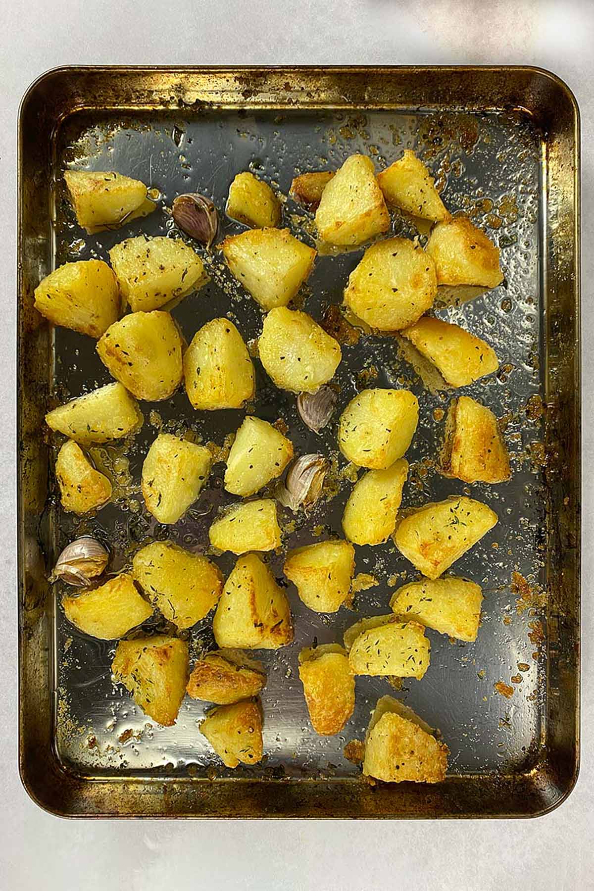 Roasted potatoes on a baking sheet with some cloves of garlic.
