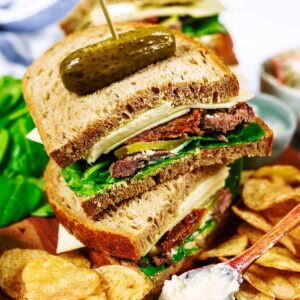 Leftover roast beef sandwich stacked up with a whole gherkin on top.