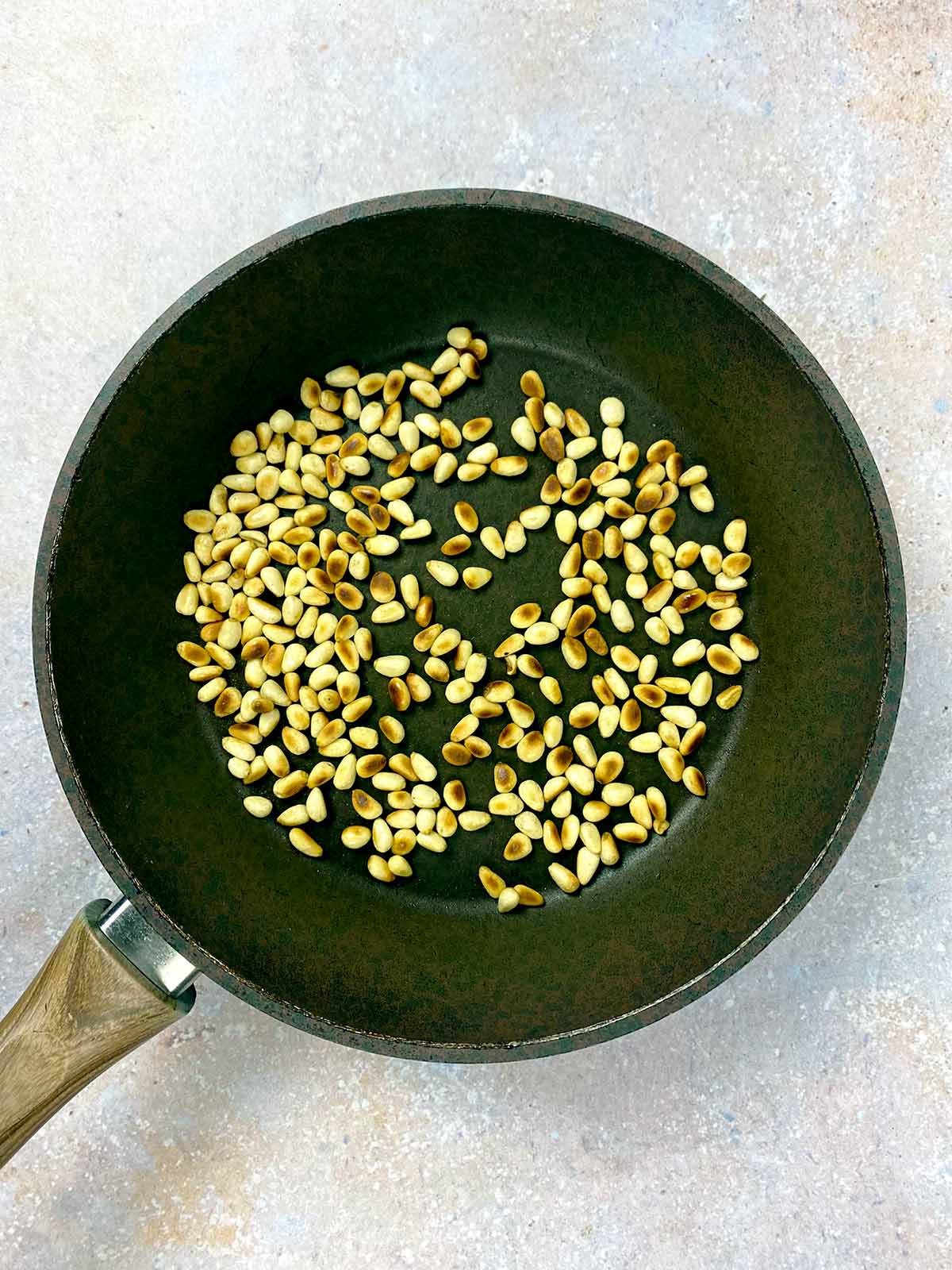 Pine nuts toasting in a frying pan.