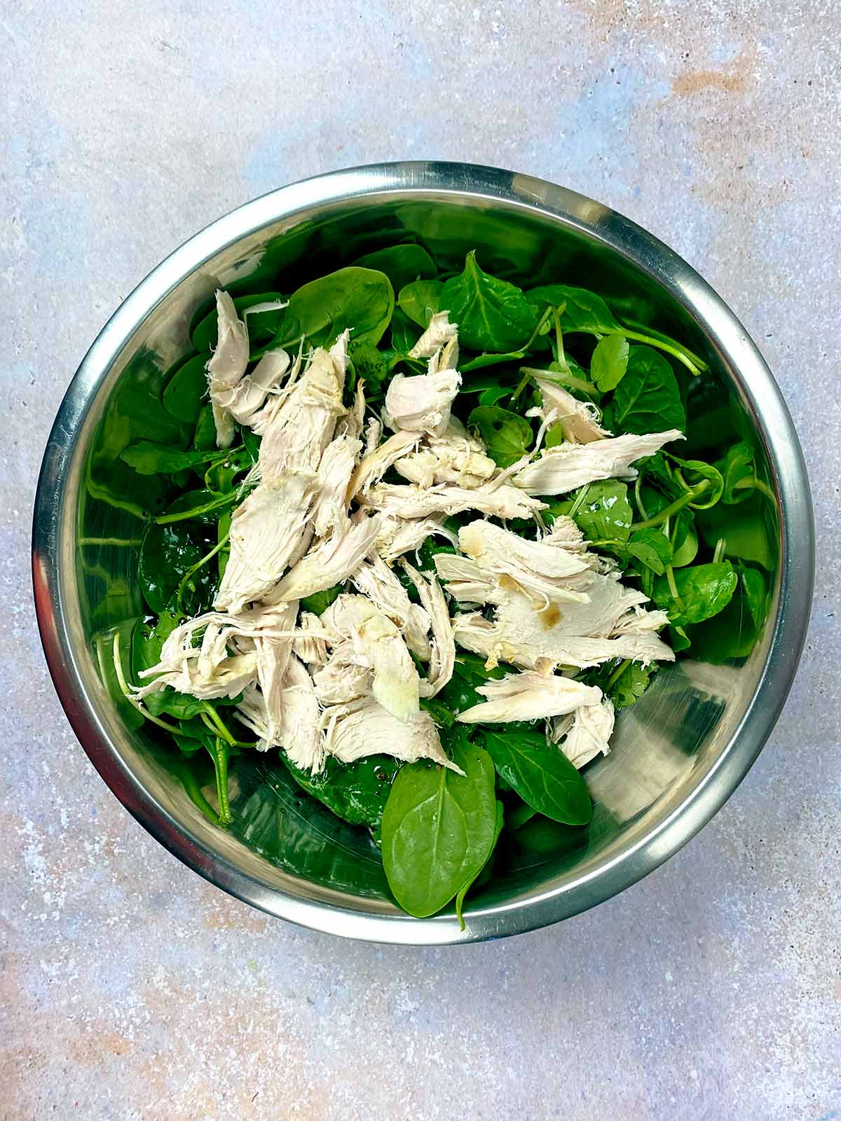 Salad leaves and shredded turkey in a metal mixing bowl.