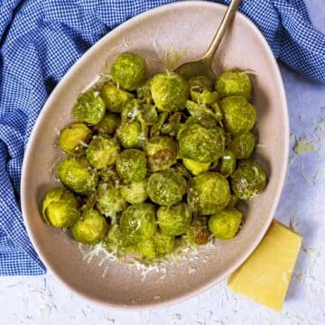 Slow Cooker Brussels Sprouts in a bowl next to a blue towel and a block of cheese.