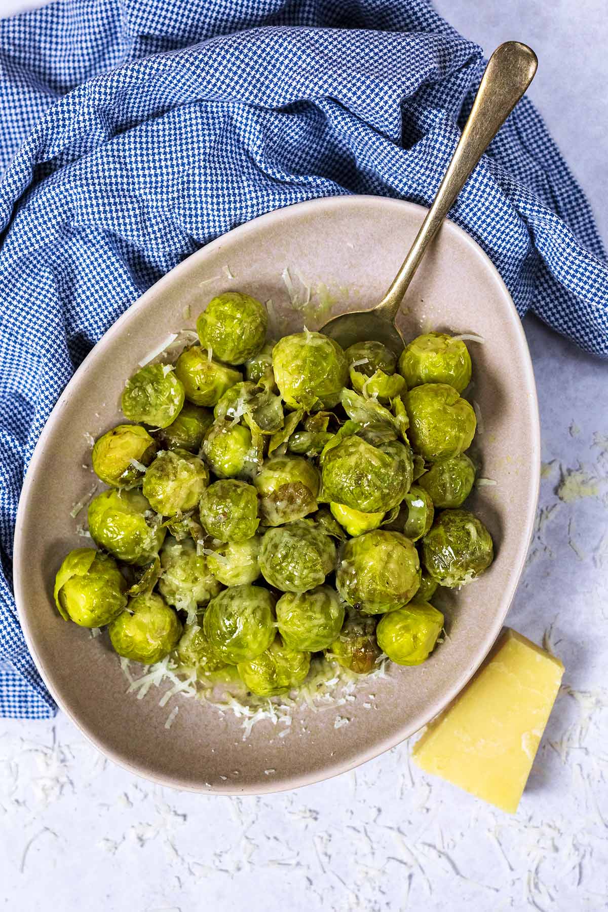 A bowl of Brussels sprouts with a spoon in front of a blue towel.