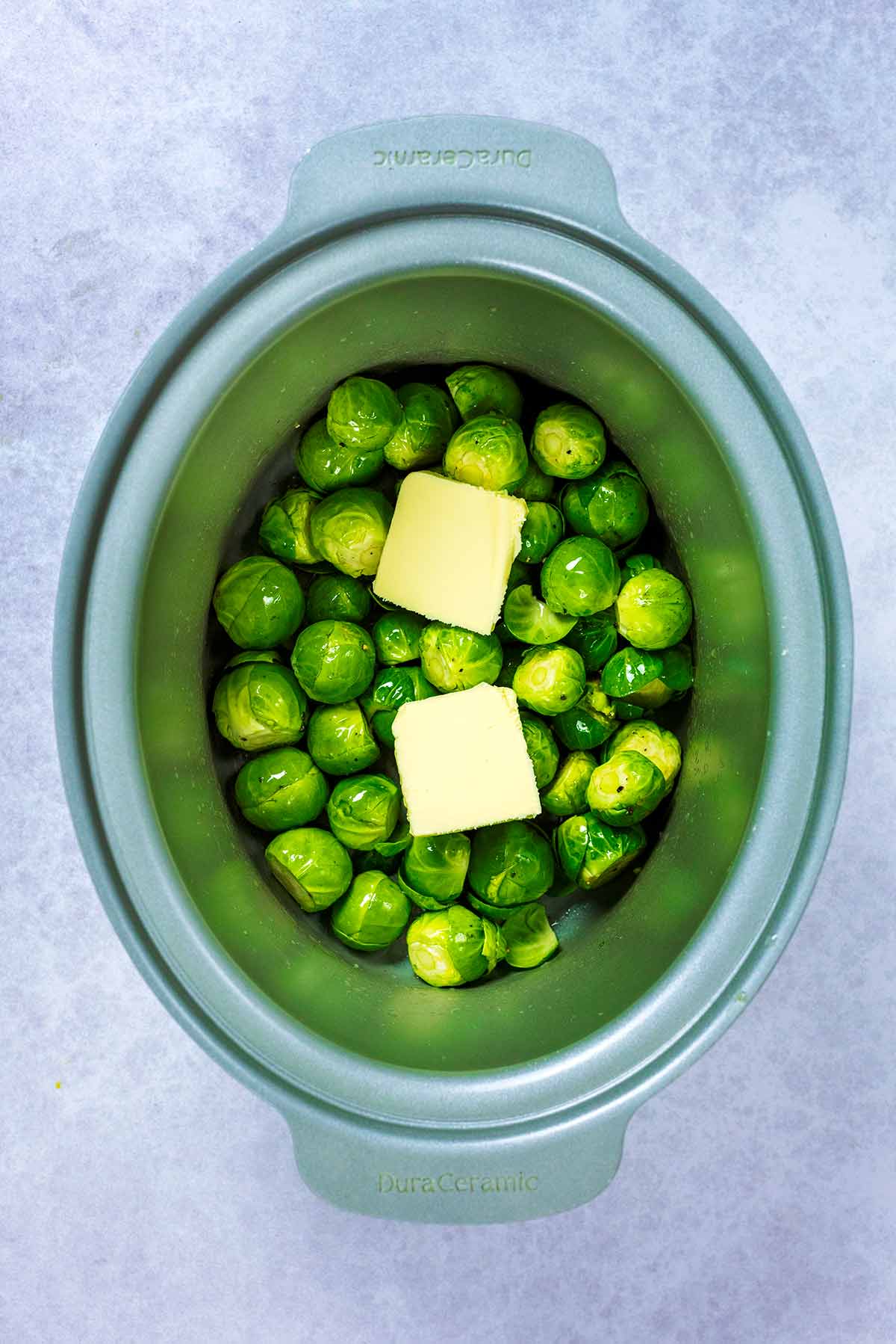 A slow cooker containing Brussels sprouts and two knobs of butter.