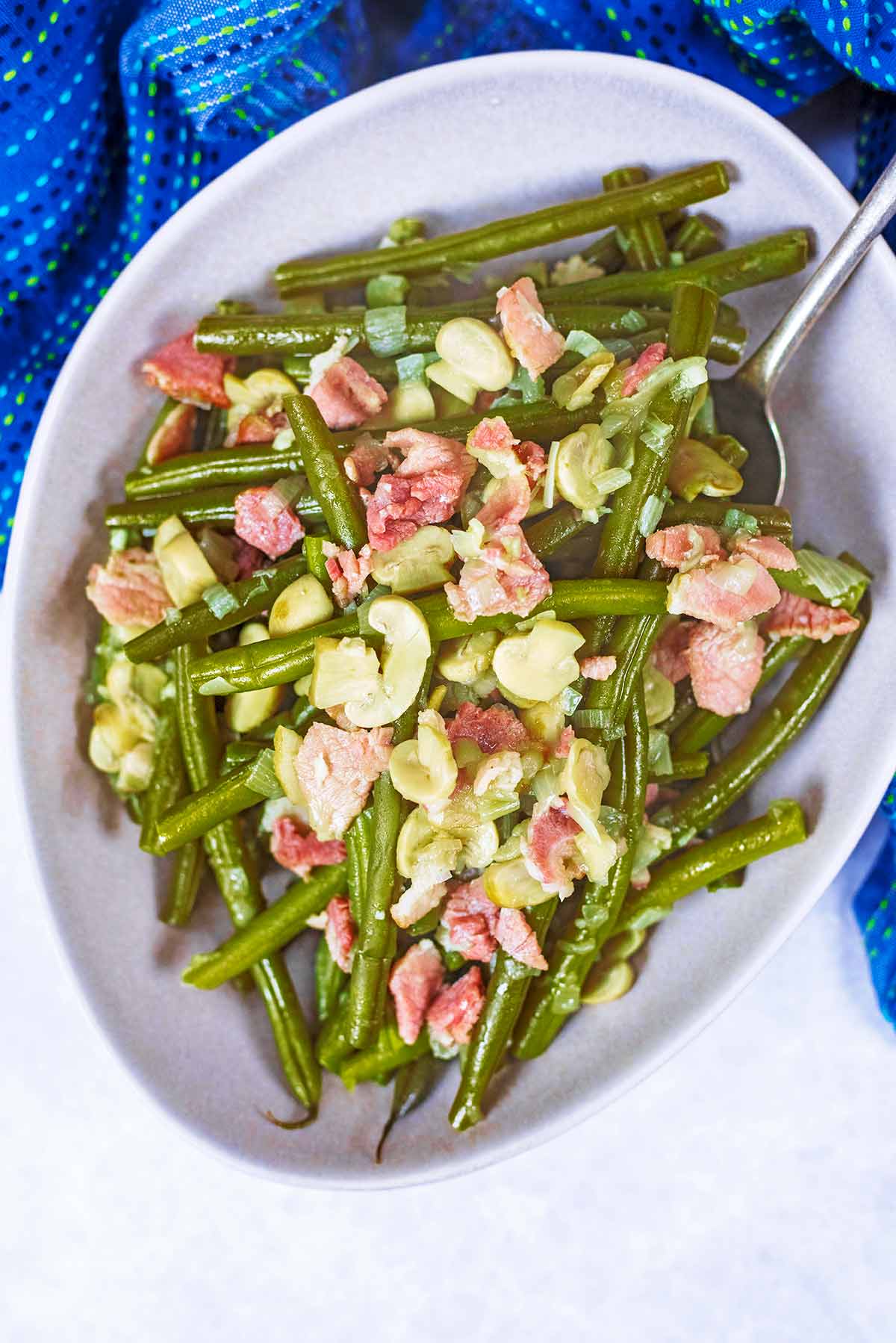 A bowl of green beans mixed with chopped bacon and sliced mushrooms.