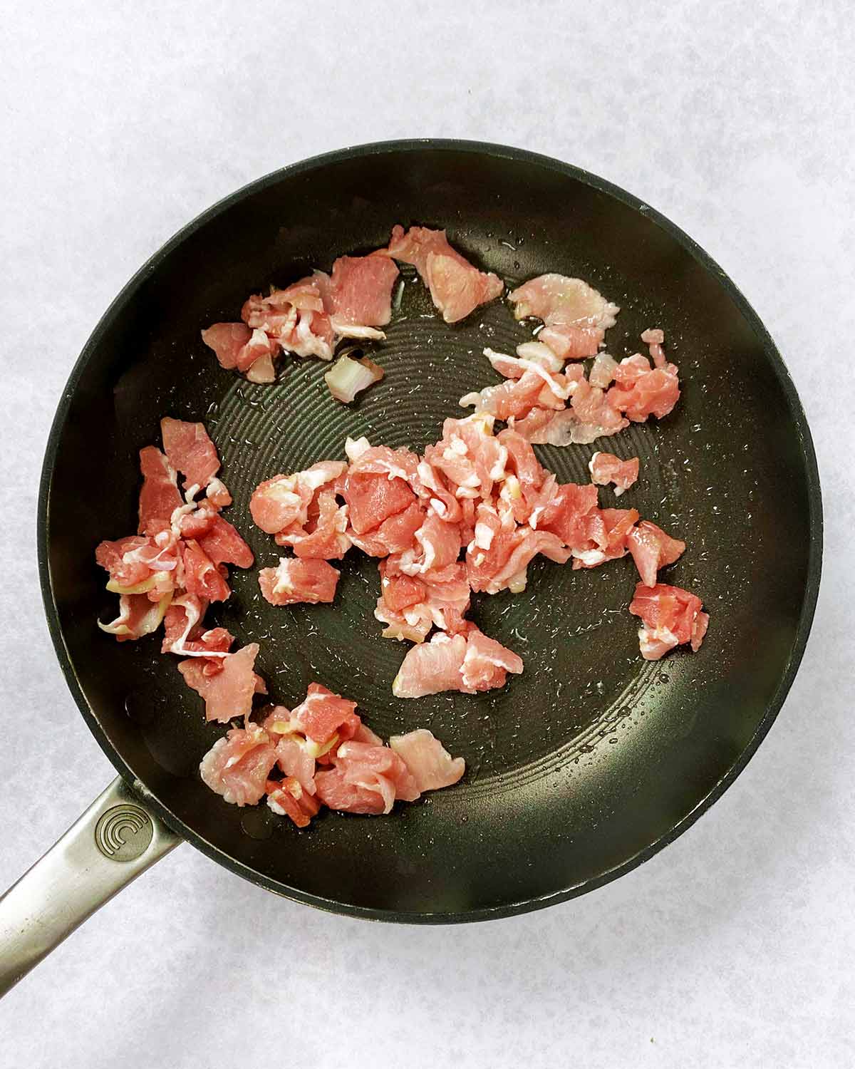 Chopped bacon cooking in a pan.