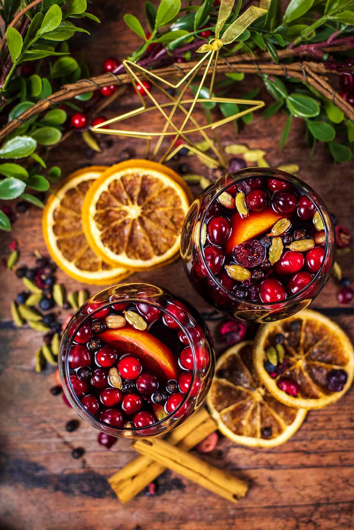 Glasses of mulled wine viewed form above next to orange slices and cinnamon sticks.