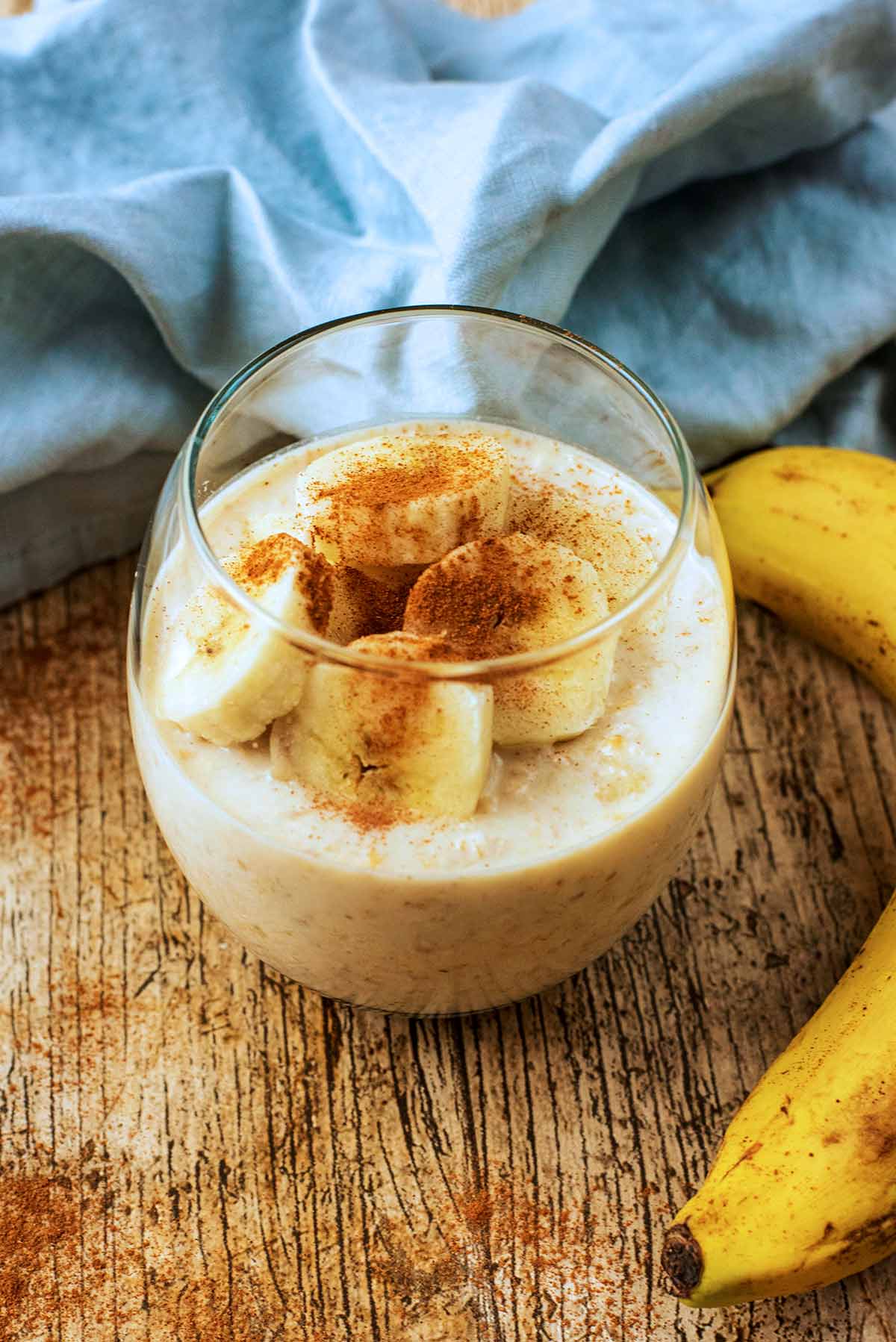 A glass of overnight oats topped with banana slices and cinnamon.