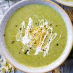 Cauliflower and broccoli soup in a bowl with cream, cheese and black pepper on top.