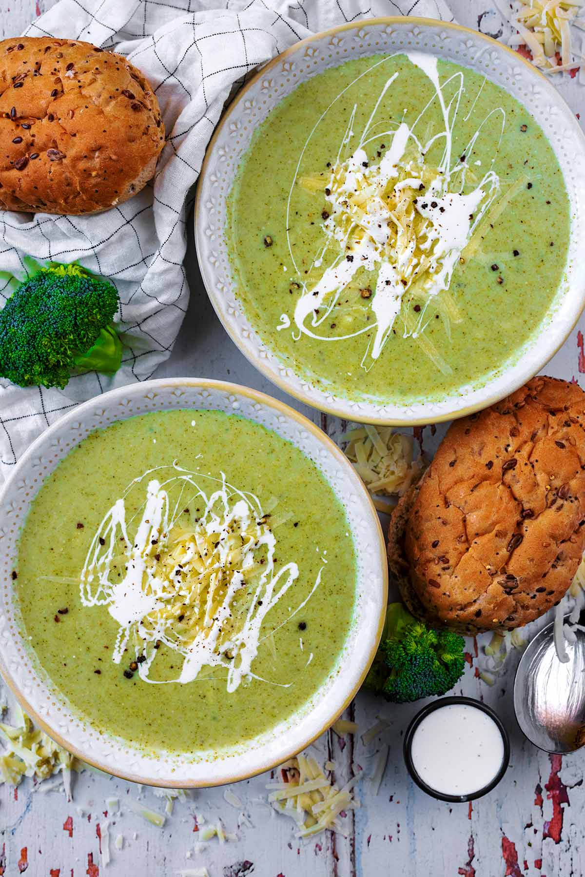 Two bowls of soup with two bread rolls next to them.
