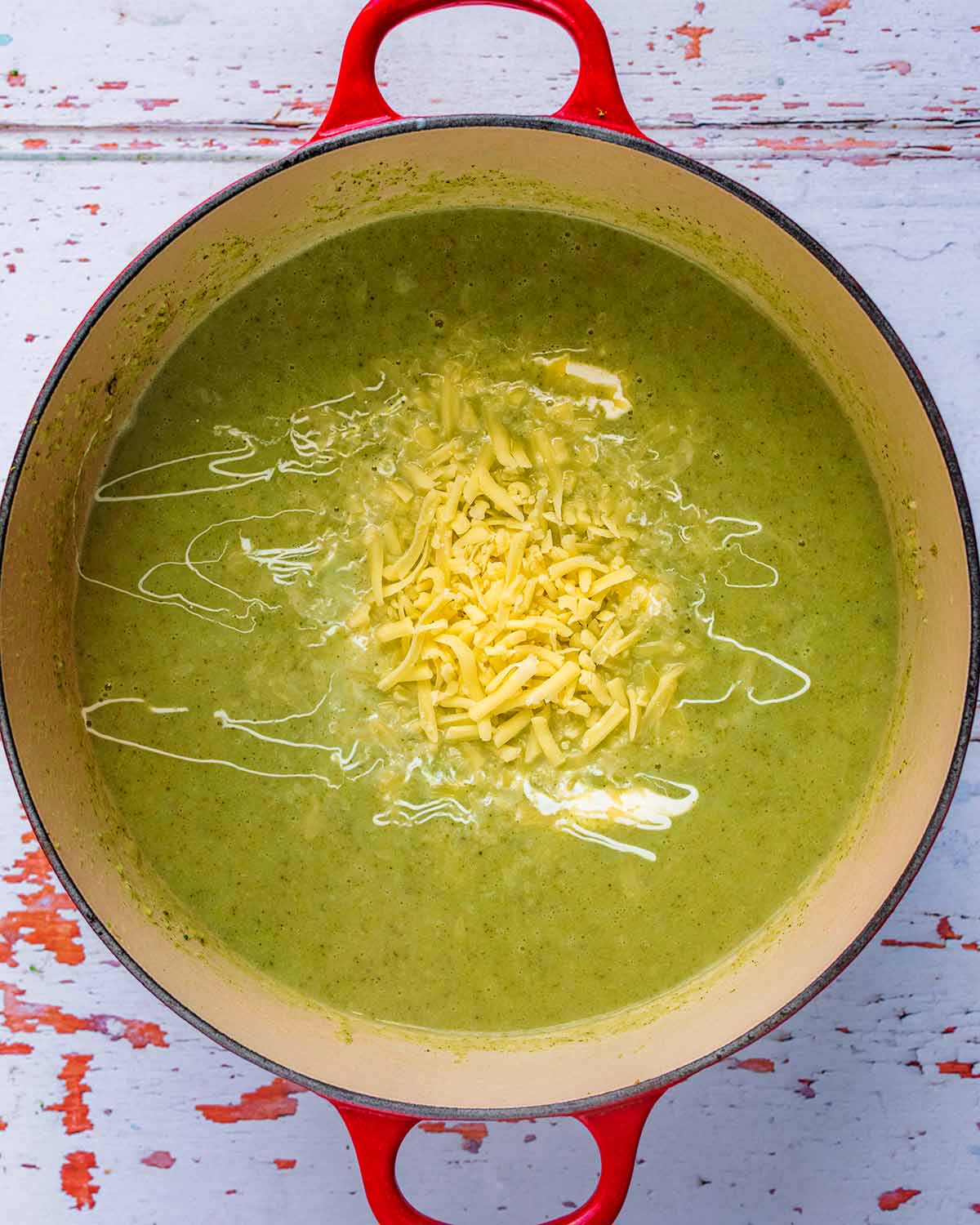 Blended soup in a large pan with cream and grated cheese on the surface.
