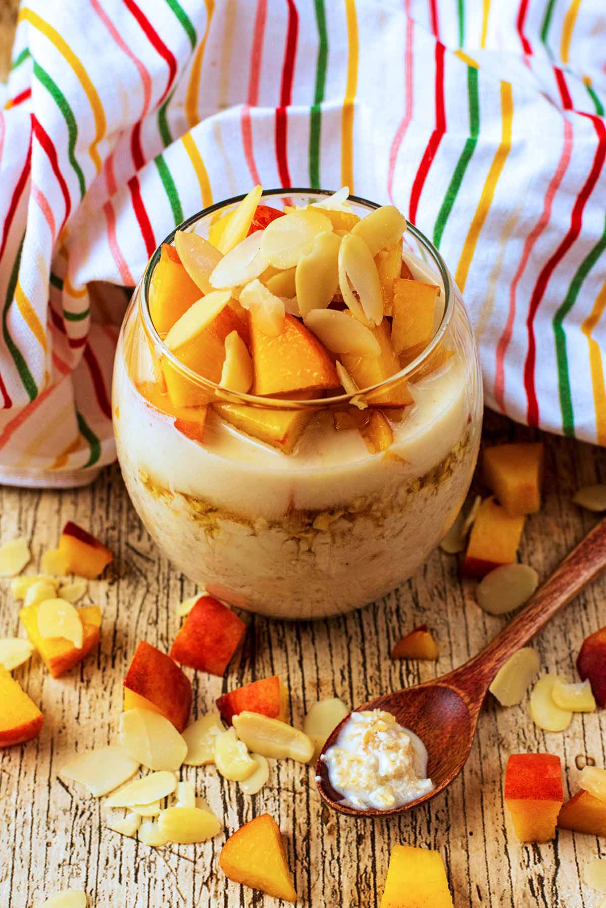 A glass of overnight oats topped with chunks of peach and almond flakes.