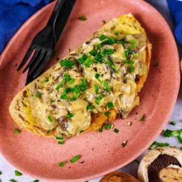 Creamy mushrooms on toast on a pink plate with a knife and fork.