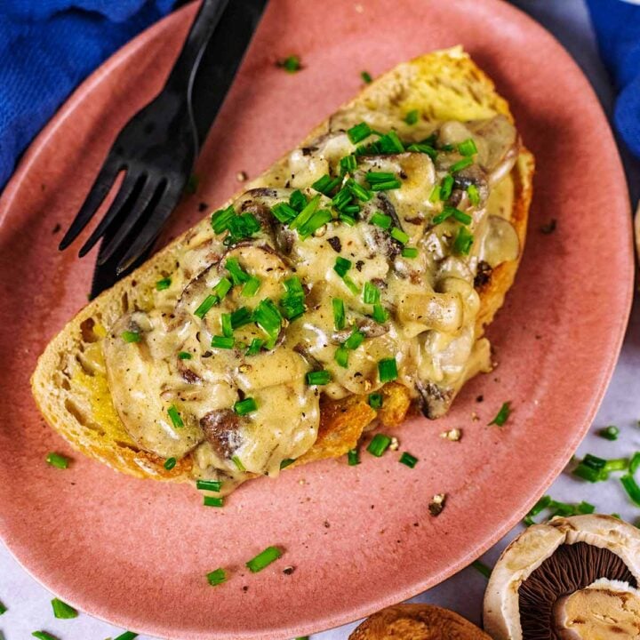 Creamy mushrooms on toast on a pink plate with a knife and fork.
