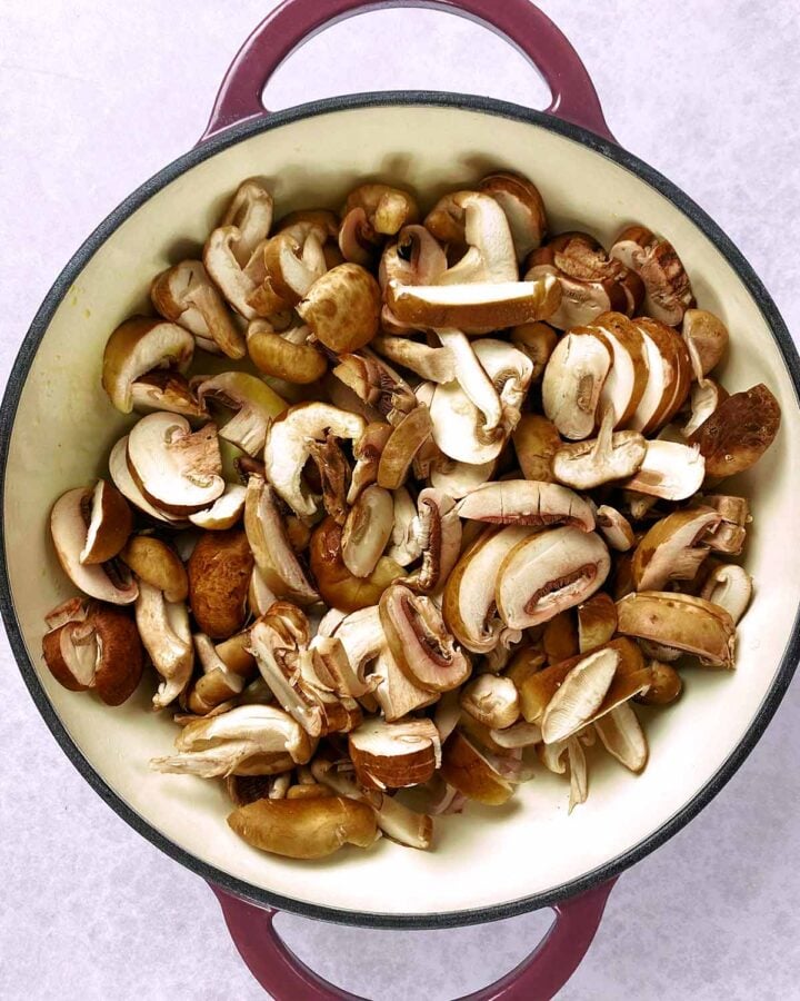 Sliced mushrooms cooking in a large pan.