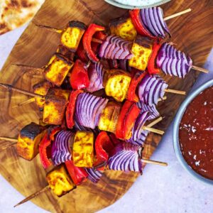 Paneer tikka skewers on a wooden serving board.